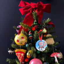 Christmas tree topped with a red bow and colorful decorations, including an M. Bubz ornament, against a dark background.